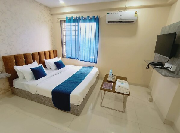 A hotel room with a bed, a television, an air conditioner, and a window with curtains.