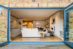 A modern interior with a white sofa, dining table, and chairs, a fireplace, and a brick wall. - Charming  Spacious 5 Bed Mews House - Kensington (Greater London)
