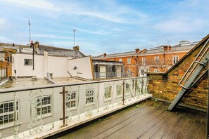 Eine Dachterrasse mit weißer Brüstung, Blick auf benachbarte Gebäude und einem klaren Himmel.