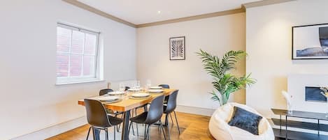 A modern dining area with a wooden table set for four, black chairs, a potted plant, and a white bean bag chair.