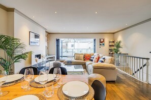 A dining area with a wooden table set for a meal, a sofa with cushions, and a staircase leading to an upper level. - Charming  Spacious 5 Bed Mews House - Kensington (Greater London)