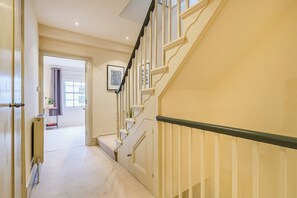 A hallway leading to a staircase with a handrail and a door on the left. - Charming  Spacious 5 Bed Mews House - Kensington (Greater London)