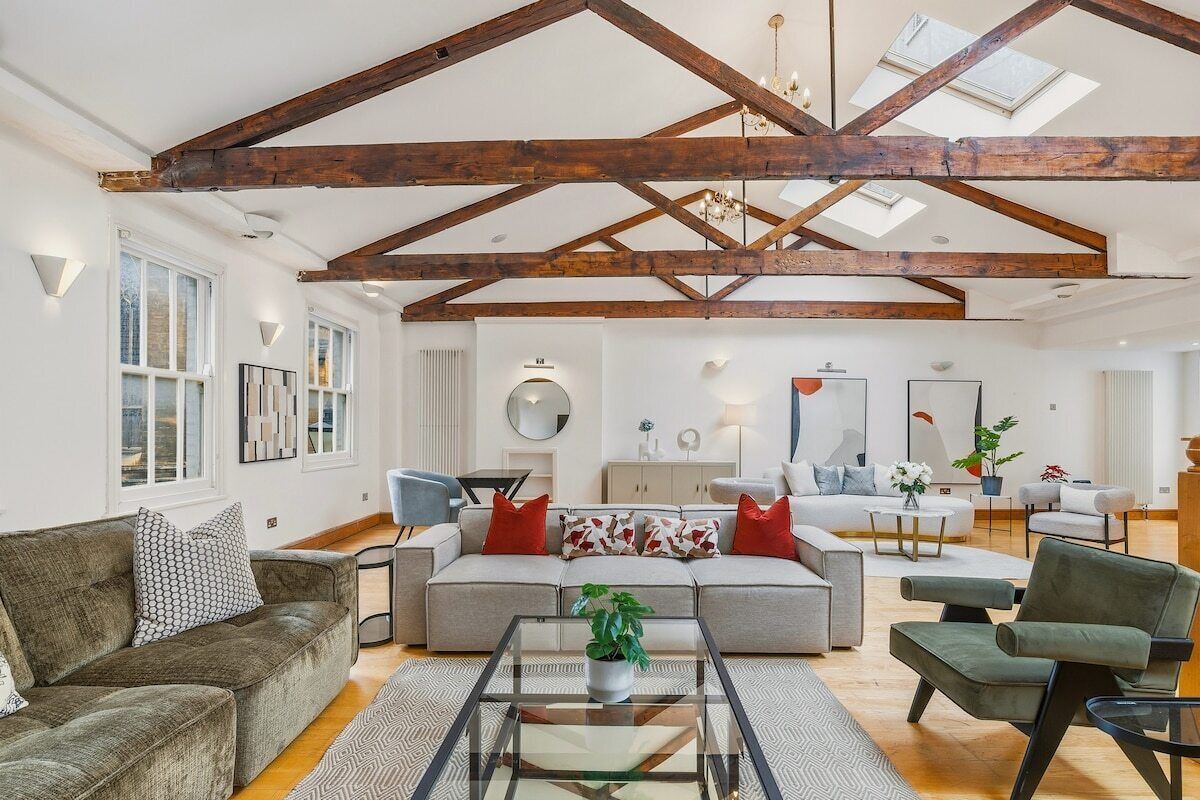 A spacious living room with a high ceiling, exposed wooden beams, and a large window providing natural light.