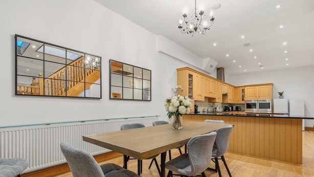 Una cocina moderna con armarios de madera, una isla central y un comedor con una mesa de madera y sillas grises.