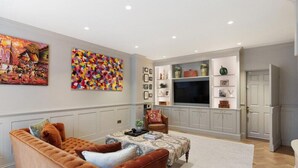 Una sala de estar con un sofá marrón, una mesa de centro y un televisor sobre un mueble bajo. Hay dos cuadros en la pared y una estantería con objetos decorativos.