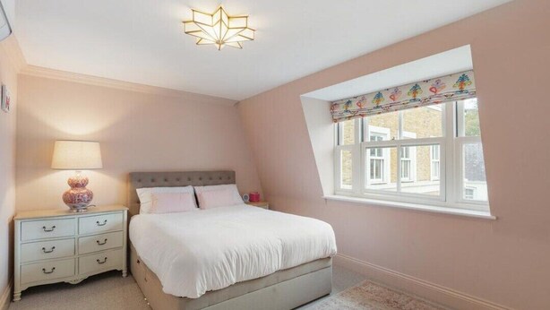 Un dormitorio con cama, mesita de noche, lámpara y ventana.