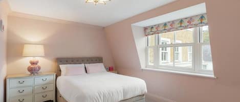Un dormitorio con cama, mesita de noche, lámpara y ventana.