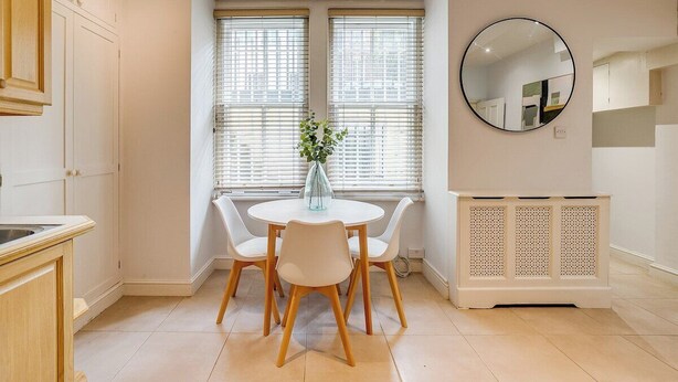 Une cuisine avec une table à manger, des chaises, un vase de fleurs et un radiateur.