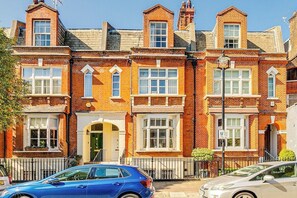 A row of red brick terraced houses with white-framed windows and a car parked in front. - Belgravia - Charming   Spacious 4 Bed Home for 9 (Greater London)