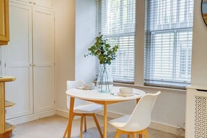 A dining area with a round table, white chairs, and a vase with a plant. - Belgravia - Charming   Spacious 4 Bed Home for 9 (Greater London)