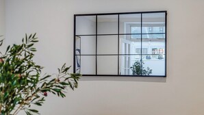 Une pièce dotée d’un grand miroir qui reflète la vue par la fenêtre, une plante et une table avec une chaise.