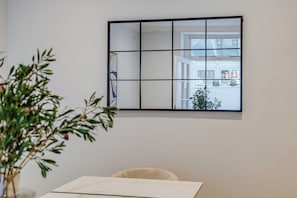 Ein Zimmer mit einem großen Spiegel, der einen Ausblick durch ein Fenster, eine Pflanze und einen Tisch mit Stuhl zeigt.