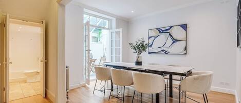 Un comedor moderno con una mesa larga y cuatro sillas, una planta en maceta y un cuadro abstracto contemporáneo en la pared.