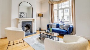 Un salon avec une cheminée, un canapé bleu et deux fauteuils blancs.