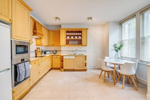 A modern kitchen with wooden cabinets, a built-in oven, and a dining area with a white table and chairs. - Belgravia - Charming   Spacious 4 Bed Home for 9 (Greater London)