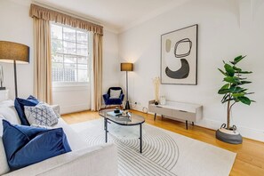 A modern living room with a sofa, coffee table, and a large window with curtains. - Belgravia - Charming   Spacious 4 Bed Home for 9 (Greater London)