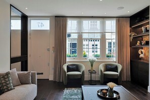 Ein modernes Wohnzimmer mit einer Couch, zwei Sesseln, einem Couchtisch und einem großen Fenster mit Vorhängen.