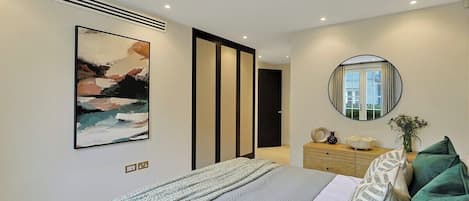 A modern bedroom with a bed, artwork, a mirror, and a dresser.