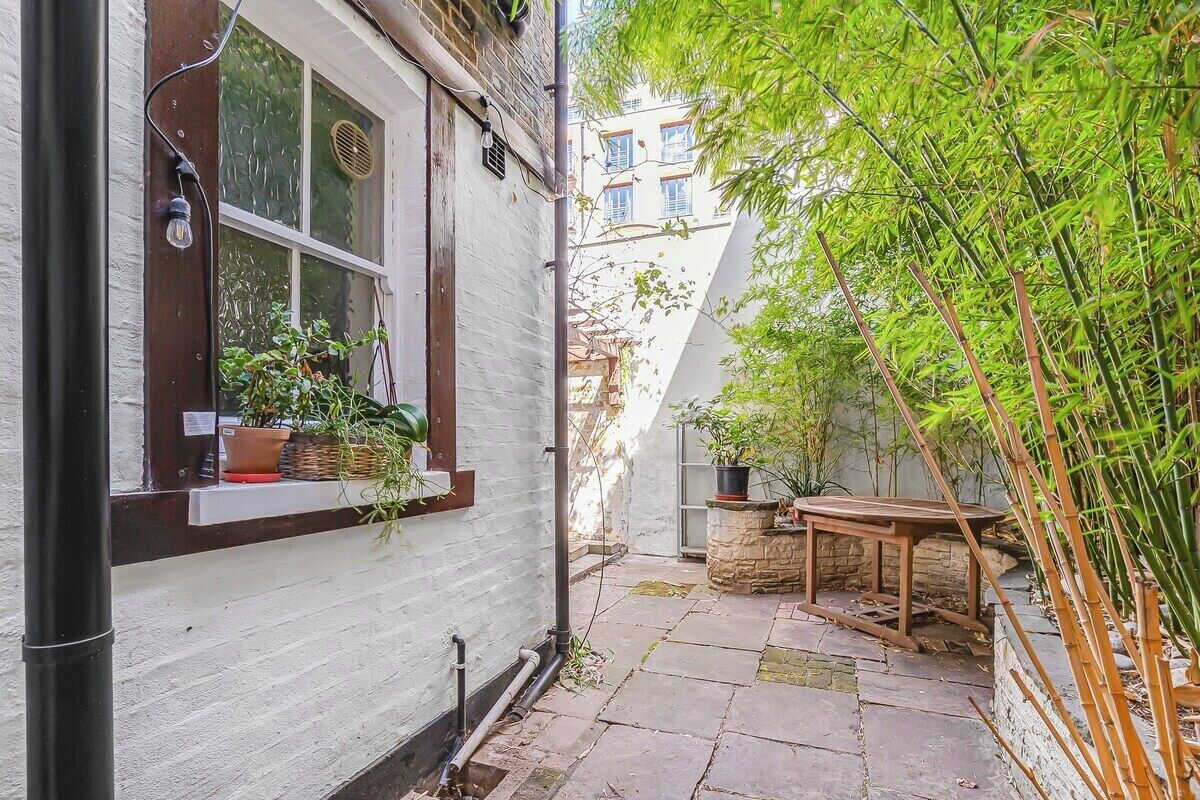 A narrow courtyard with a white building, a wooden table, and bamboo plants.