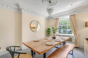 Un coin repas avec une table en bois dressée pour quatre personnes, un banc, un miroir et une fenêtre avec des rideaux.