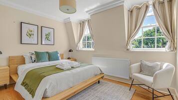 A bedroom with a bed, bedside tables, a chair, a window with curtains, and framed pictures on the wall.