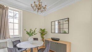 Un comedor con una mesa redonda, sillas grises, un jarrón con plantas, una consola de madera y un espejo en la pared.