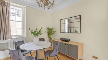 A dining area with a round table, grey chairs, a vase with plants, a wooden console table, and a mirror on the wall.