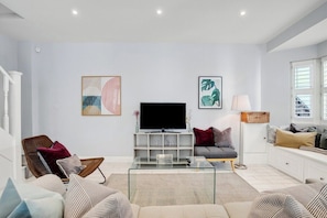 Ein modernes Wohnzimmer mit Flachbildfernseher, bequemen Sitzmöglichkeiten und Kunstwerken an den Wänden.