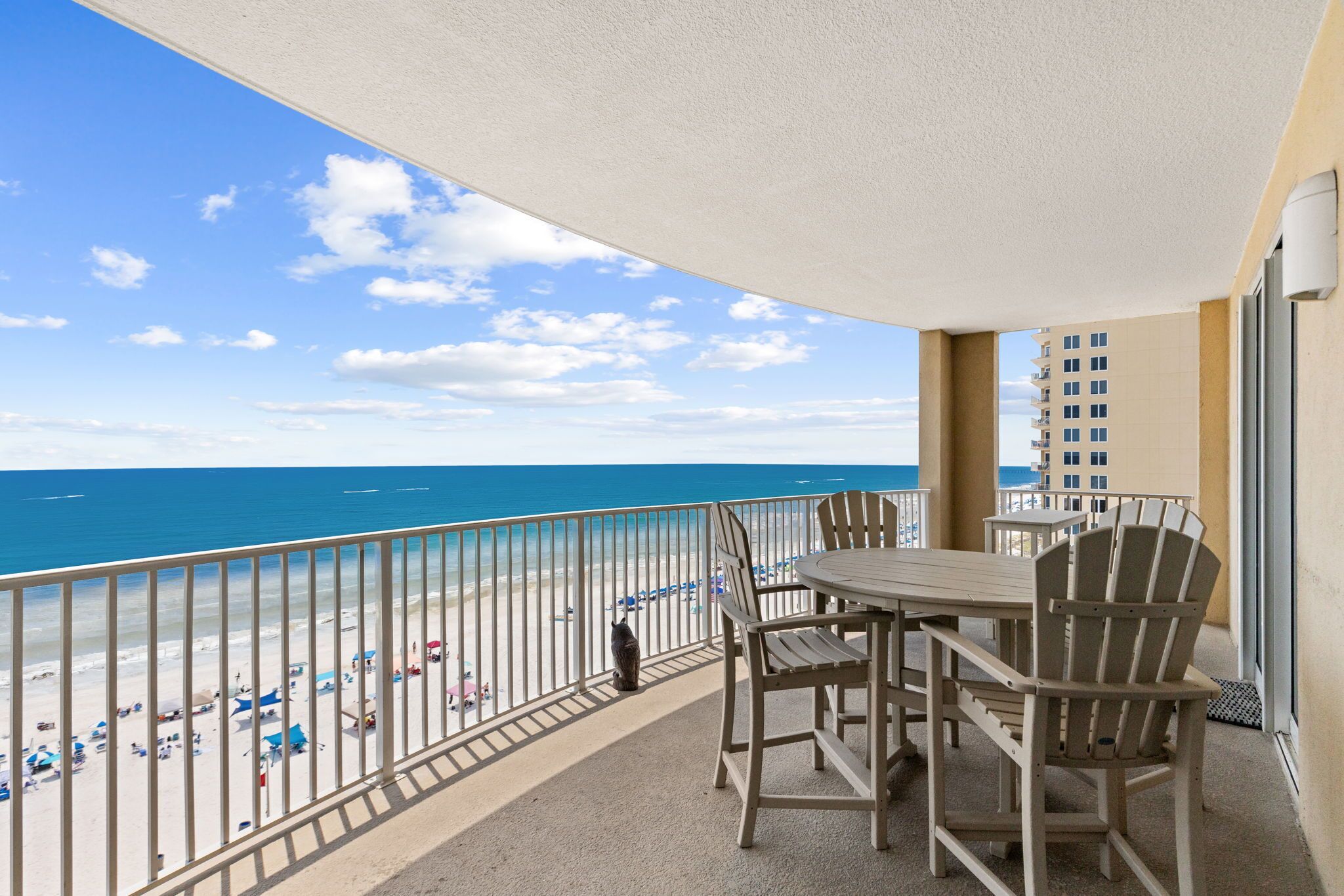 A balcony with a view of the beach and ocean, featuring a table and chairs, and a railing.