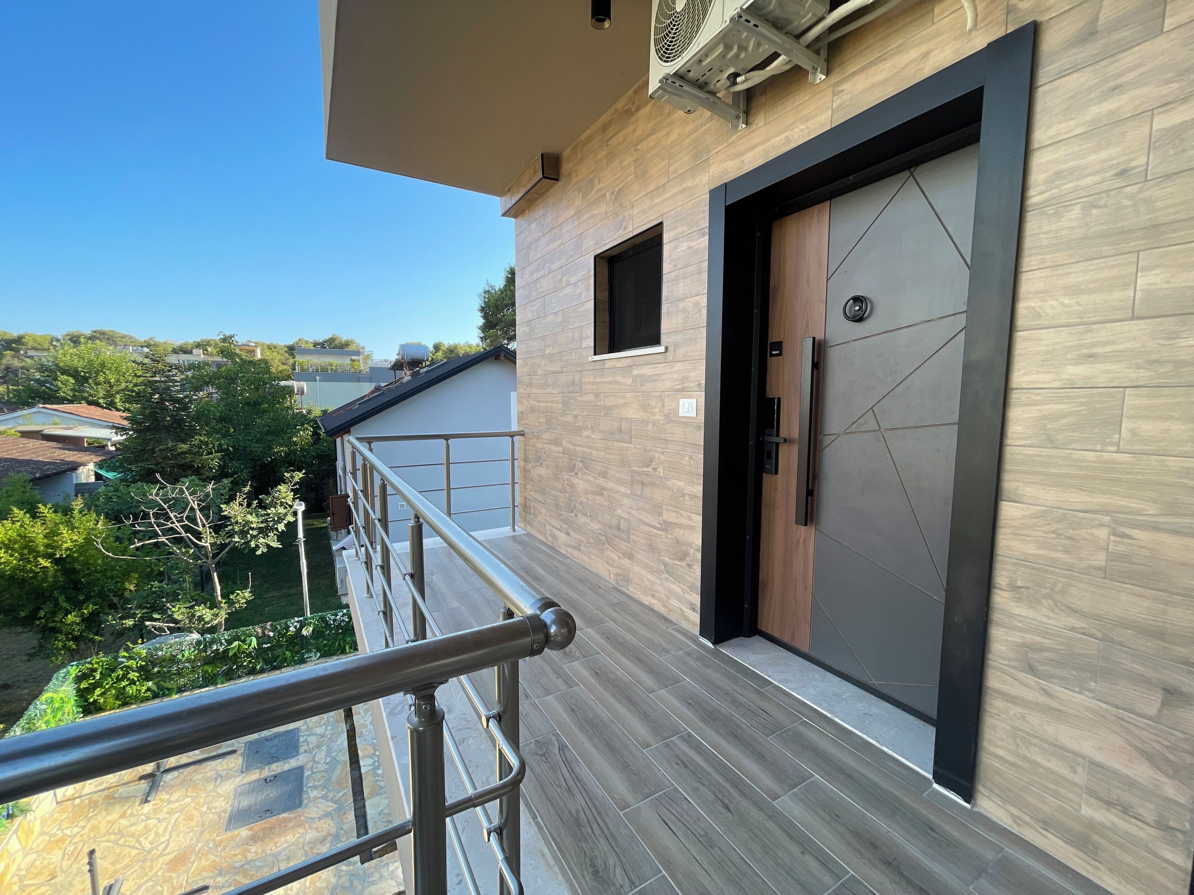 A modern building with a balcony, a door with a keypad lock, and a view of the surrounding neighborhood.