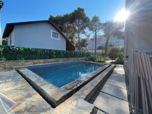 Una piscina con baldosas de piedra, rodeada por un muro y un seto de piedra.