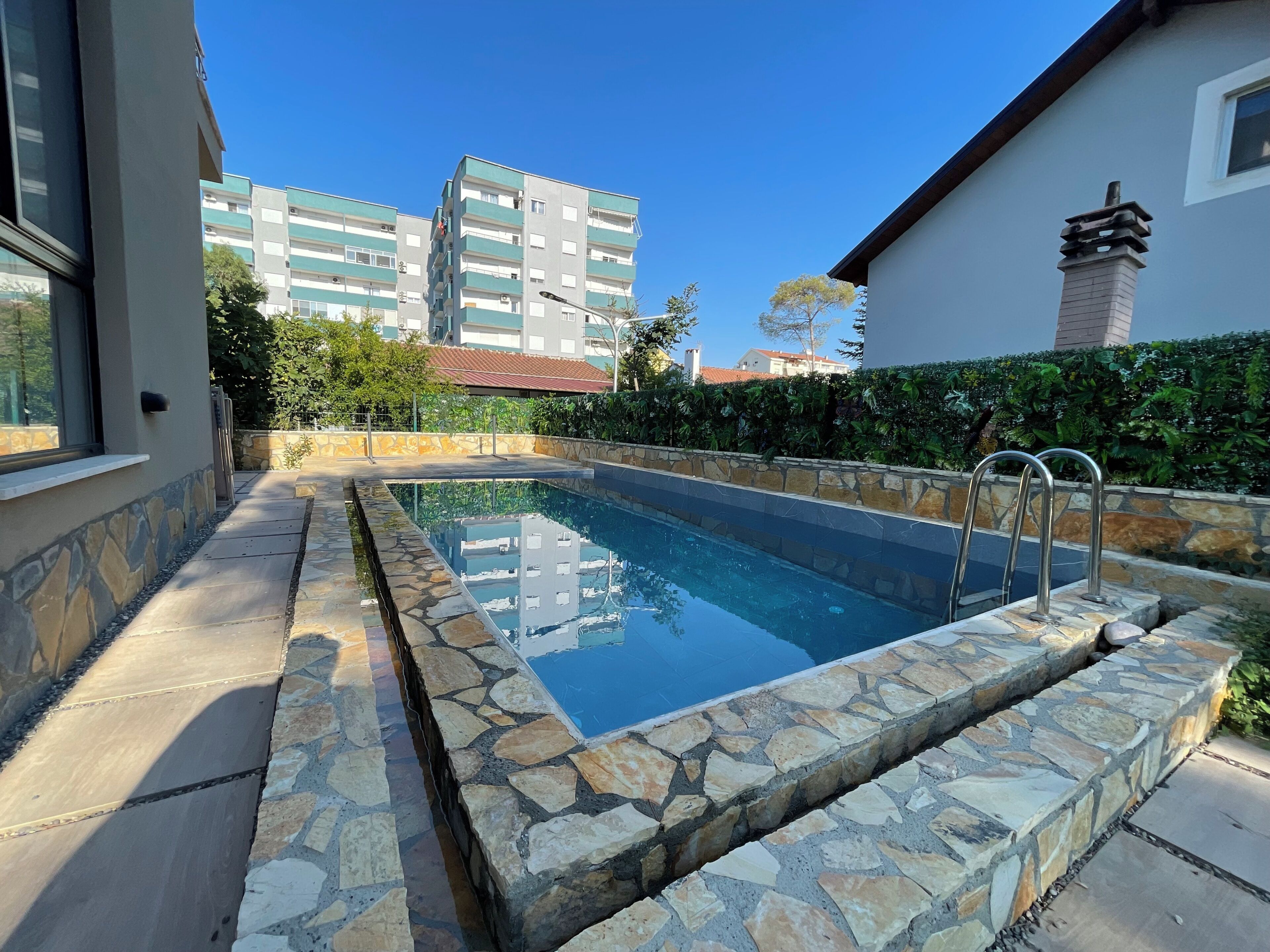 Piscina con borde de piedra, barandilla de metal y pared de piedra.