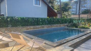 Uma piscina com espreguiçadeiras, um muro de pedra e um edifício ao fundo.