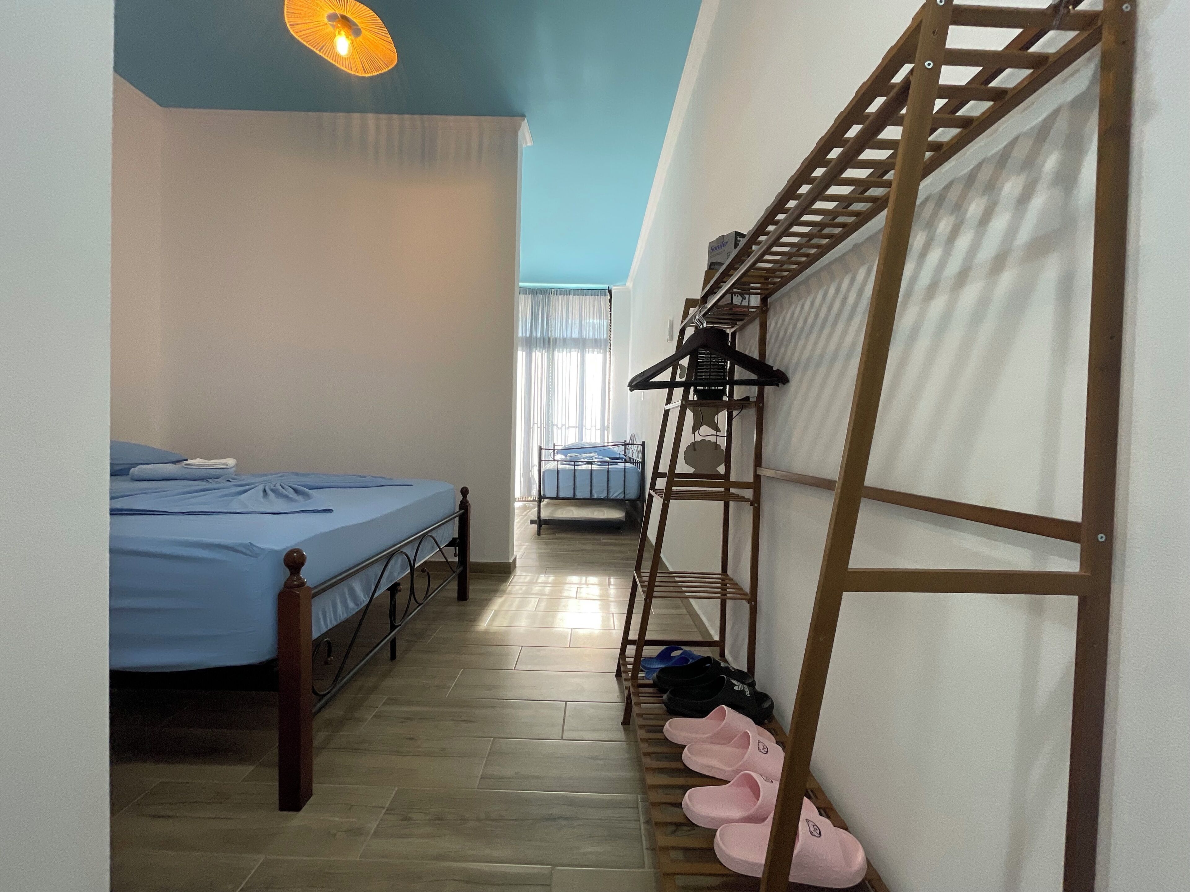 Una habitación pequeña con una cama, un zapatero y una ventana con cortinas.