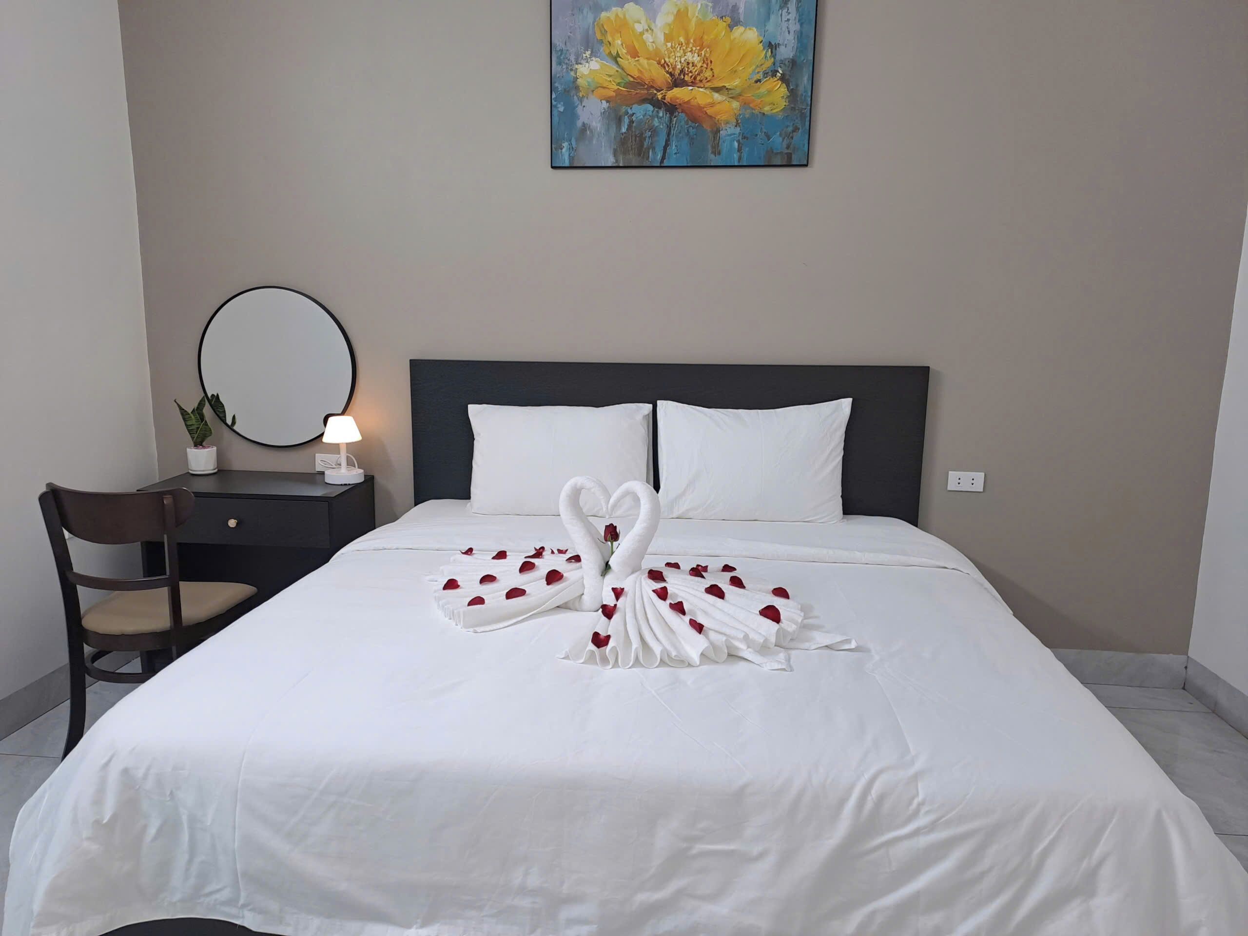A hotel room with a neatly made bed, a bedside table with a lamp, a chair, and a painting on the wall.