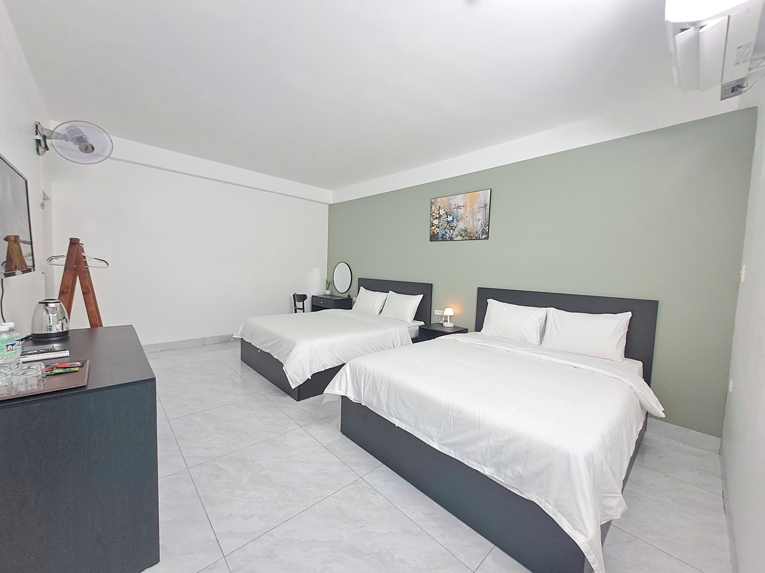 Habitación de hotel con dos camas, un escritorio, una silla, una lámpara y un cuadro en la pared.