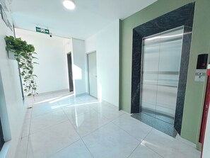 A clean, modern hallway with a shiny tiled floor, a green wall, and an elevator with a marble accent.