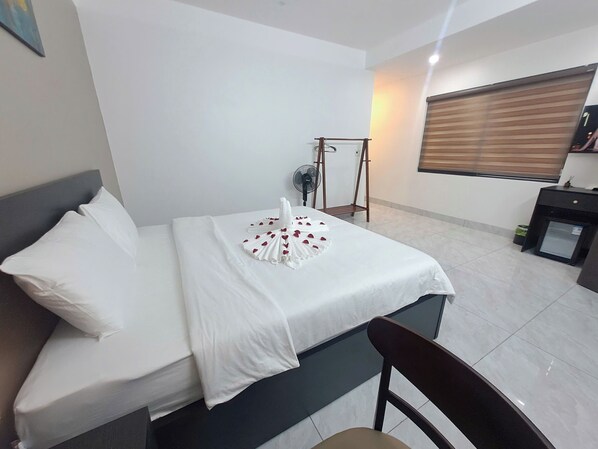 A hotel room with a bed, a chair, a desk, a fan, and a window with blinds.