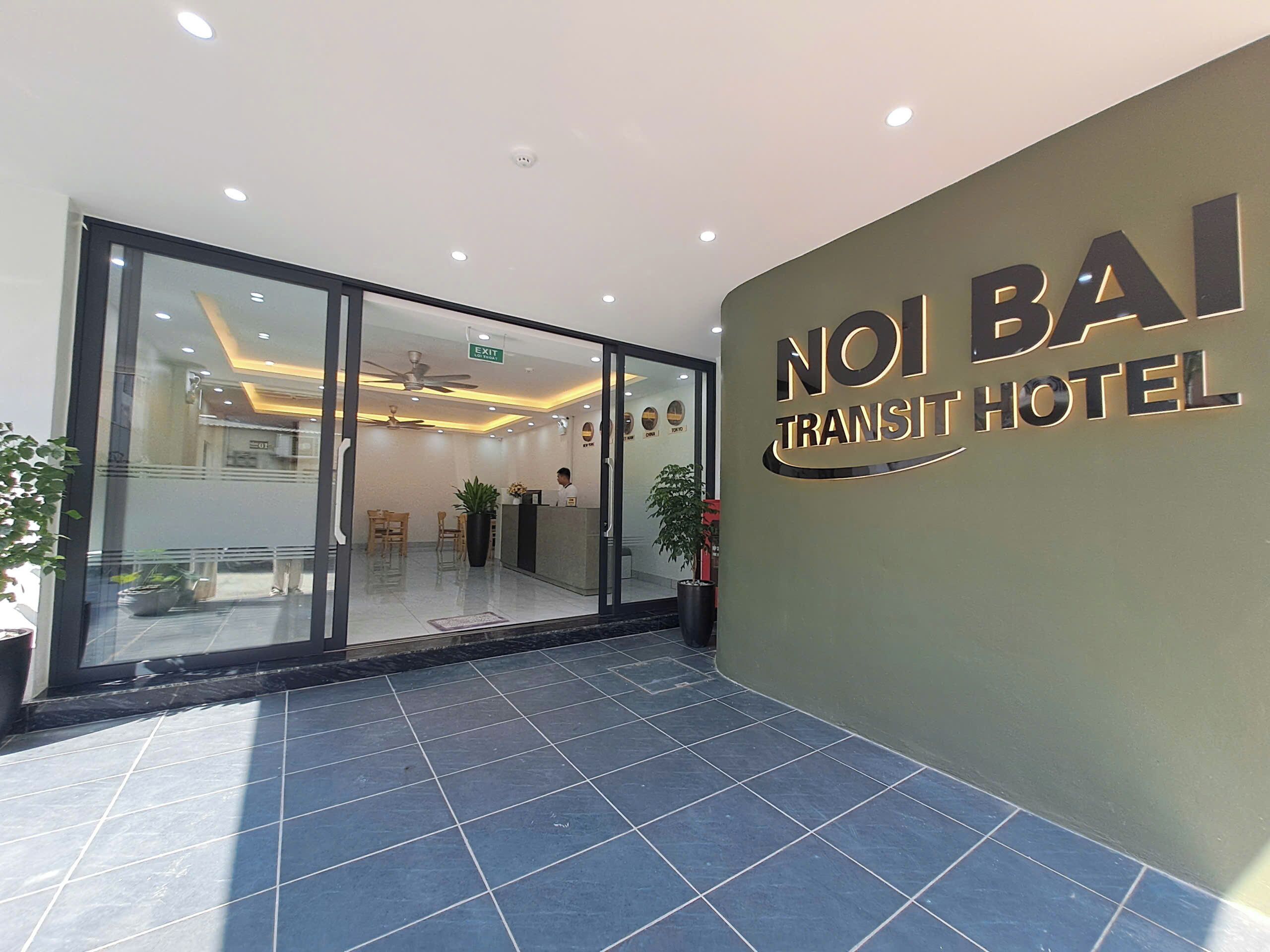 The entrance to Noi Bai Transit Hotel with a reception desk, seating area, and a clear glass door.