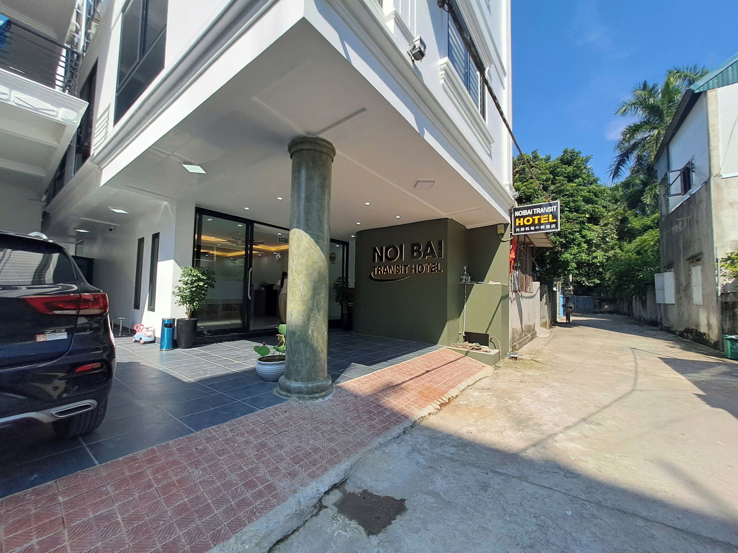 The entrance of Noibai Transit Hotel with a tiled pavement, a parked car, and a signboard.