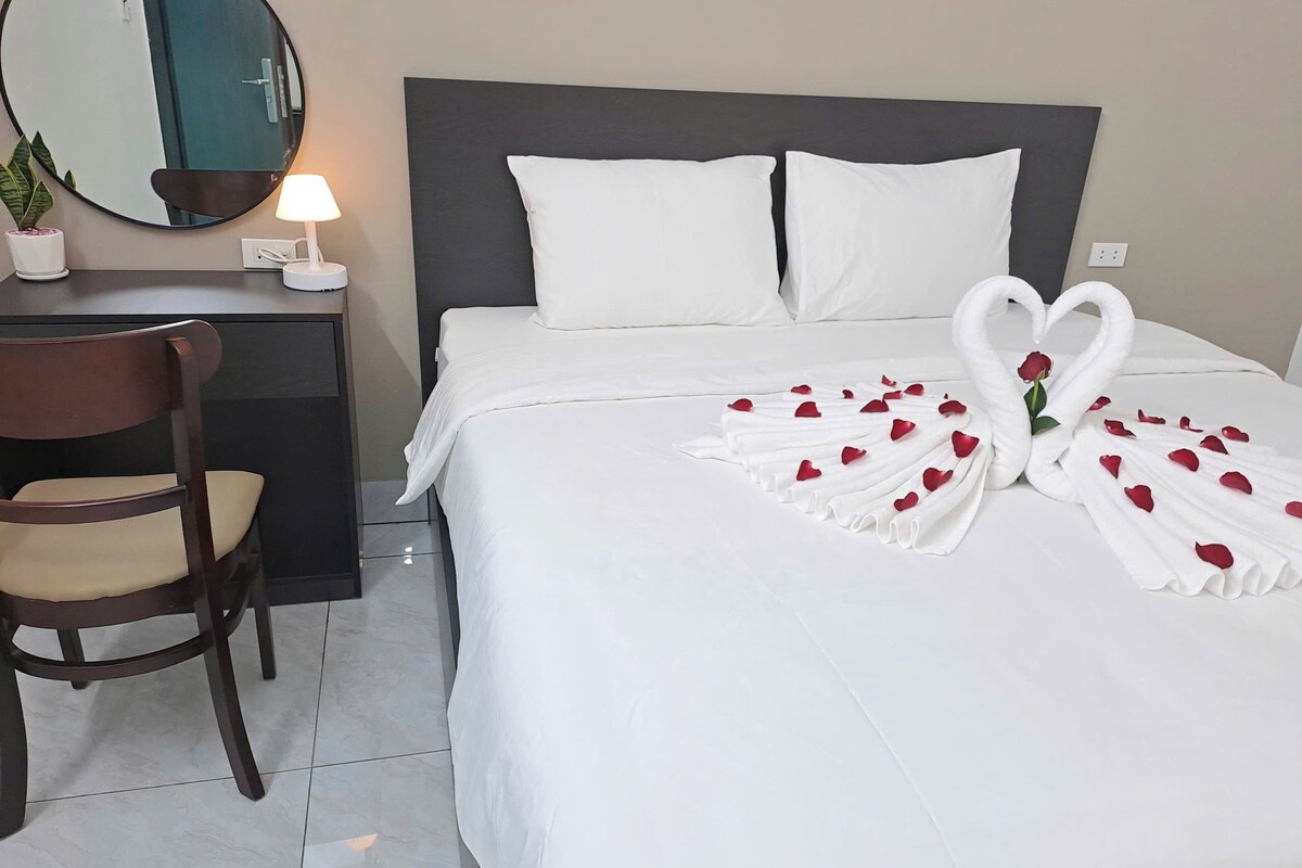 Habitación de hotel con una cama bien hecha, una silla, un escritorio, una lámpara y un espejo.