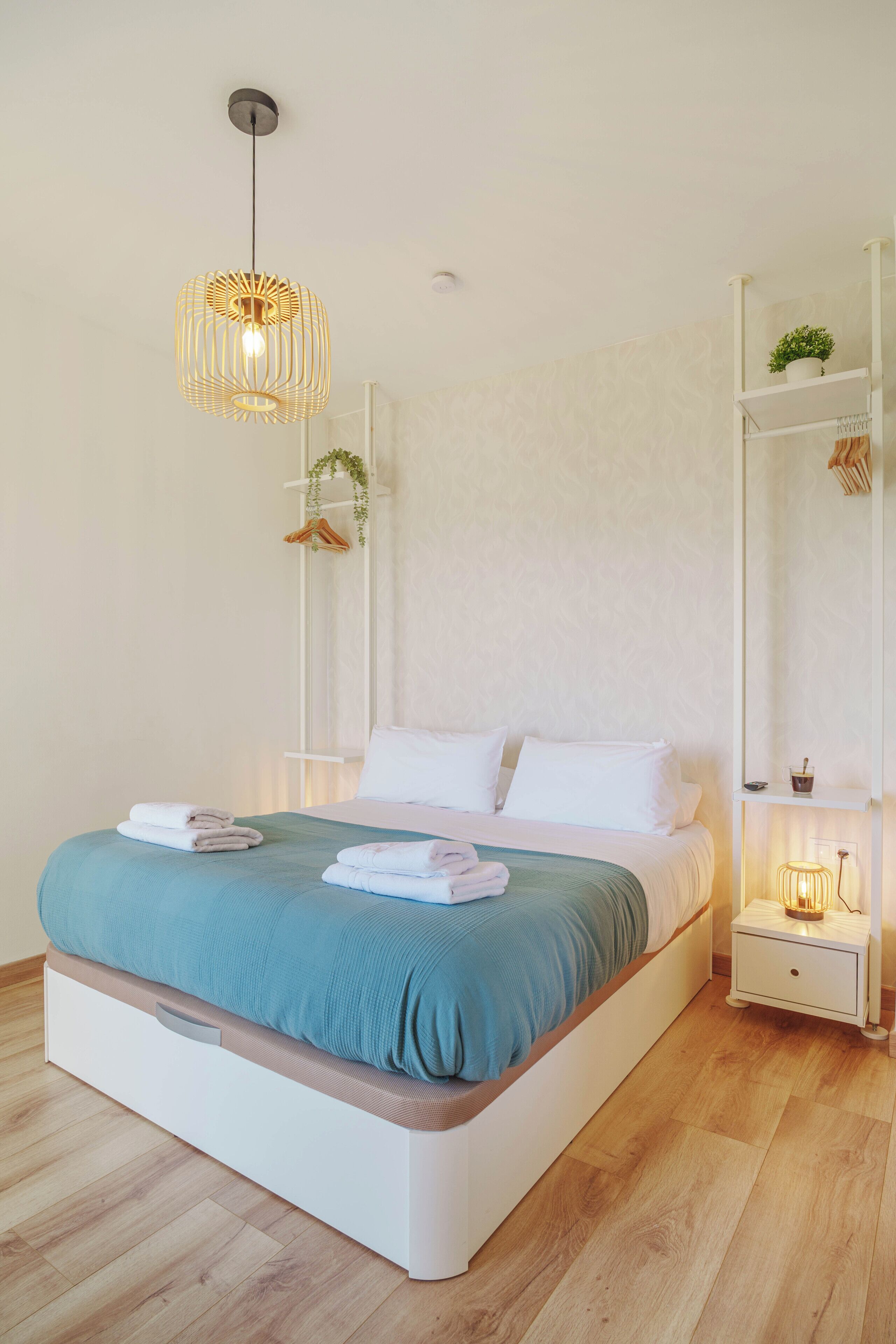 A modern bedroom with a bed, bedside tables, a hanging light fixture, and a wall-mounted shelf with a plant.