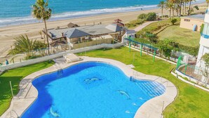 A swimming pool with a curved edge, surrounded by a grassy area and a view of the beach and ocean. - Marbella Beach Front View by Sol Maestranza (Marbella)