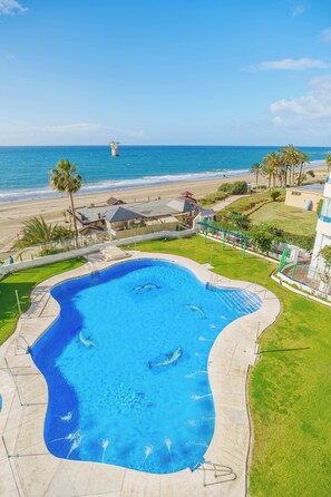 Ein Pool mit geschwungener Kante, umgeben von einer Rasenfläche und Blick auf den Strand und das Meer.