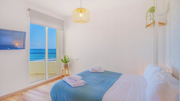 A bedroom with a bed, a TV, a plant, and a view of the ocean. - Marbella Beach Front View by Sol Maestranza (Marbella)
