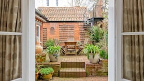 An open doorway leading to a courtyard with a brick building, a wooden table, and potted plants. - Aldeburgh - spacious 3 bed period house on High St (Aldeburgh)