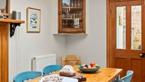 A dining area with a wooden table, blue chairs, a fruit bowl, and a book. - Aldeburgh - spacious 3 bed period house on High St (Aldeburgh)