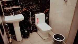 A bathroom with a white sink, toilet, and a black trash bin. - HOTEL DIBYANSH PREMIUM (Bhubaneshwar)