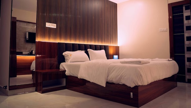 A modern bedroom with a large bed, a wooden headboard, a bedside table, and a built-in wardrobe. - HOTEL DIBYANSH PREMIUM (Bhubaneshwar)