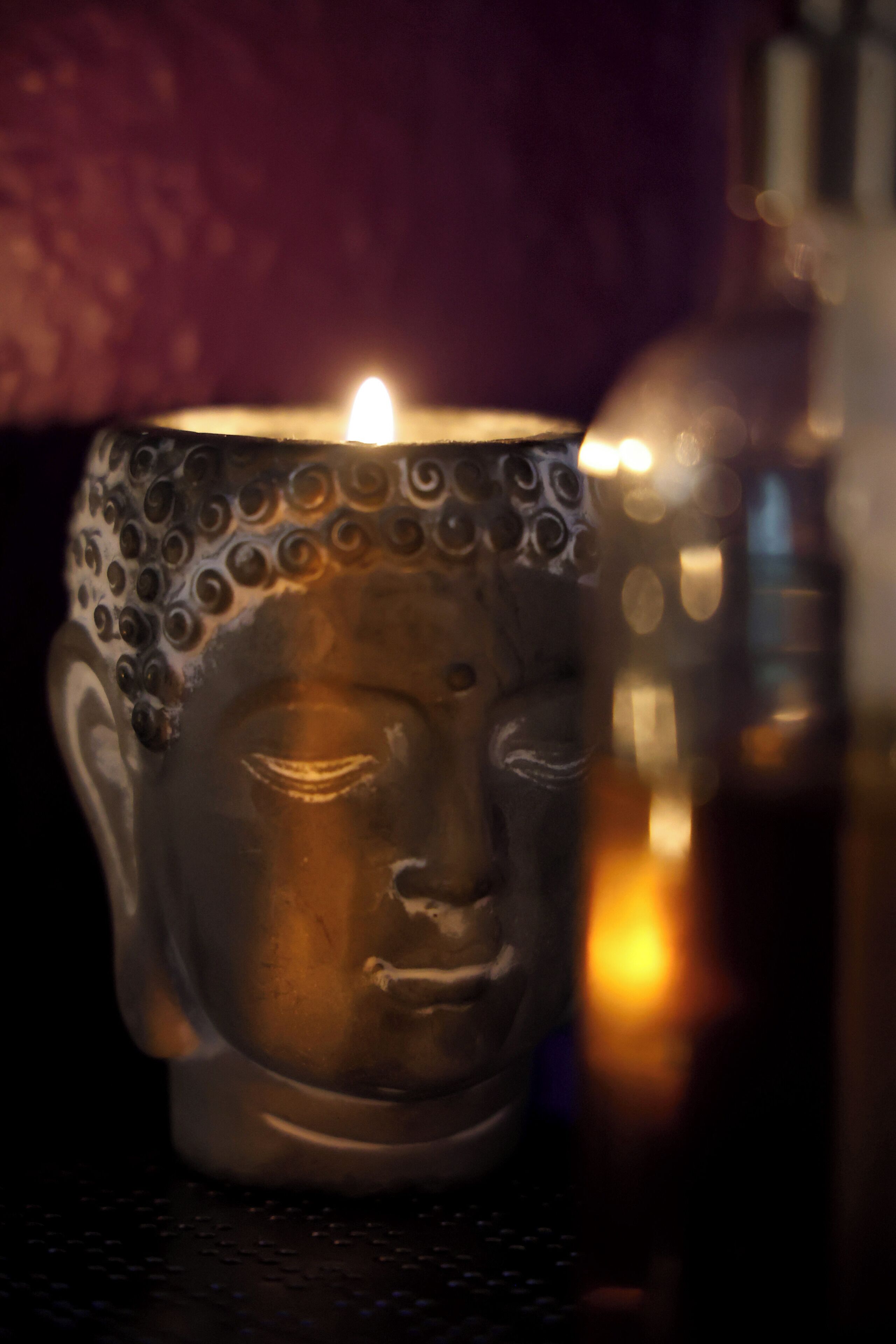 A candle in a decorative holder with a Buddha-like face.